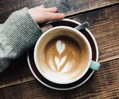 overhead-vertical-shot-person-s-hand-near-latte-art-coffee-wooden-surface.jpg